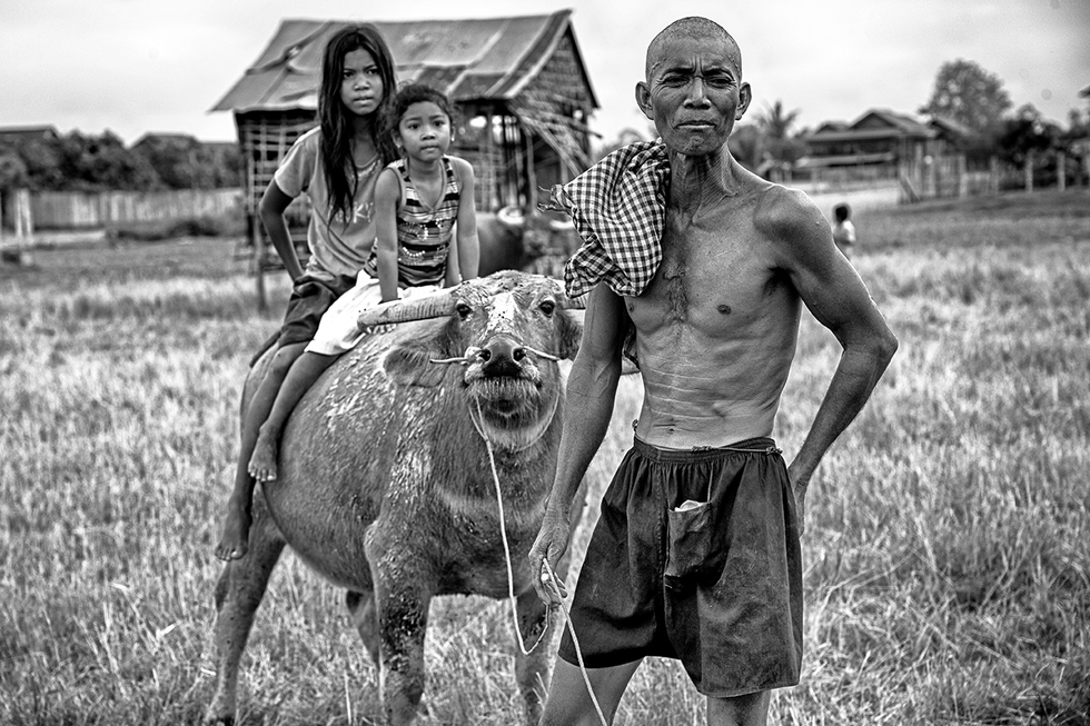 Black and white photo of a man and children riding a water buffalo in a rural setting, capturing daily life and family ties — a heartfelt moment by Cristian Mitrani.
