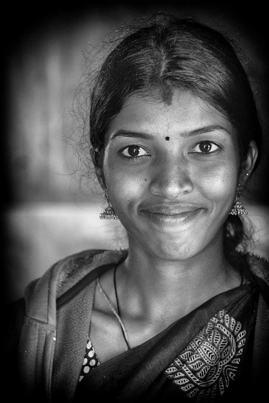 Black and white close-up portrait of a smiling young woman with traditional jewelry and a bindi, radiating warmth — a vibrant cultural moment captured by Cristian Mitrani.