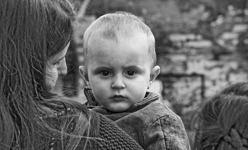 Black and white portrait of a serious-looking baby in a woman's arms, gazing directly at the camera — a poignant moment captured by Cristian Mitrani.