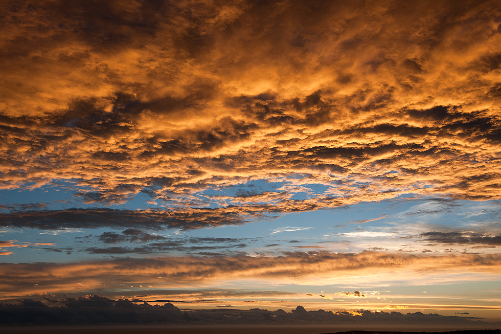 A breathtaking landscape featuring a vibrant sunset sky with dramatic orange and pink clouds, casting warm light over a vast, natural scenery. This scene reflects Cristian Mitrani's artistic focus on capturing the beauty and power of nature's landscapes