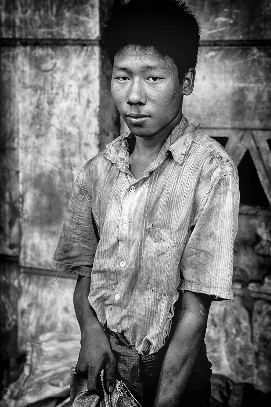 Black and white portrait of a young man wearing a worn shirt, standing against a textured wall with a serious and reflective expression — a poignant moment captured by Cristian Mitrani.