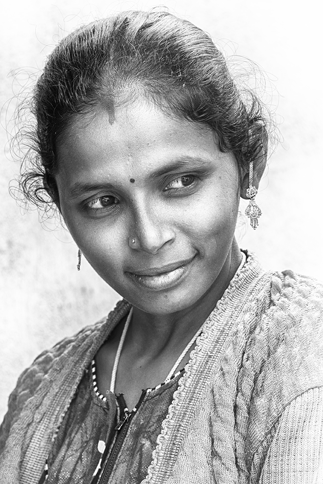 Black and white portrait of a young woman looking to the side with a subtle smile, adorned with traditional earrings and a bindi — a graceful cultural capture by Cristian Mitrani.
