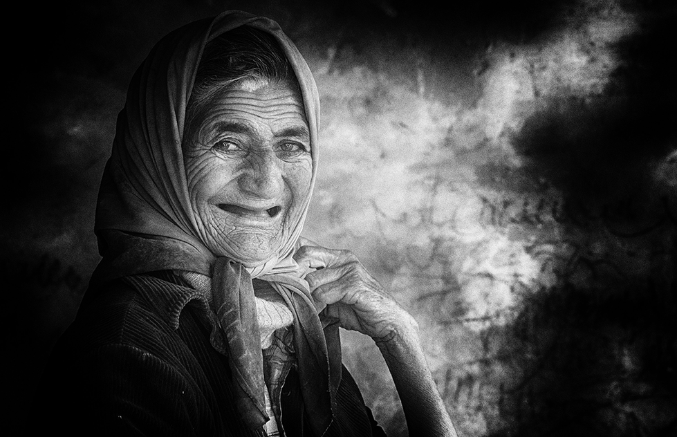 Black and white portrait of a smiling elderly woman wearing a headscarf, her eyes bright with warmth — a heartfelt and intimate capture by Cristian Mitrani.