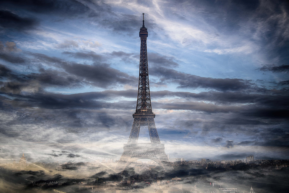 An atmospheric photograph of the Eiffel Tower in Paris, shrouded in mist and dramatic clouds, showcasing Cristian Mitrani's skill in capturing moody, evocative scenes of iconic landmarks. The image emphasizes the tower's grandeur amidst a mysterious, moody sky.
