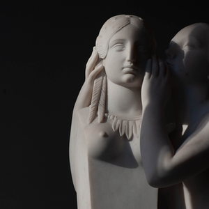 Softly lit white sculpture of two classical figures, one whispering to the other, against a dark background — a serene and intimate artwork by Cristian Mitrani.