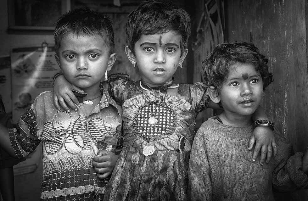 Black and white portrait of three young children standing close together, each with distinct expressions conveying innocence and resilience — a heartfelt moment captured by Cristian Mitrani.