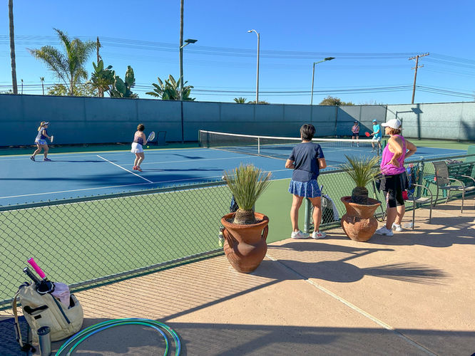 two people watch as a doubles match is played at Meridian Tennis