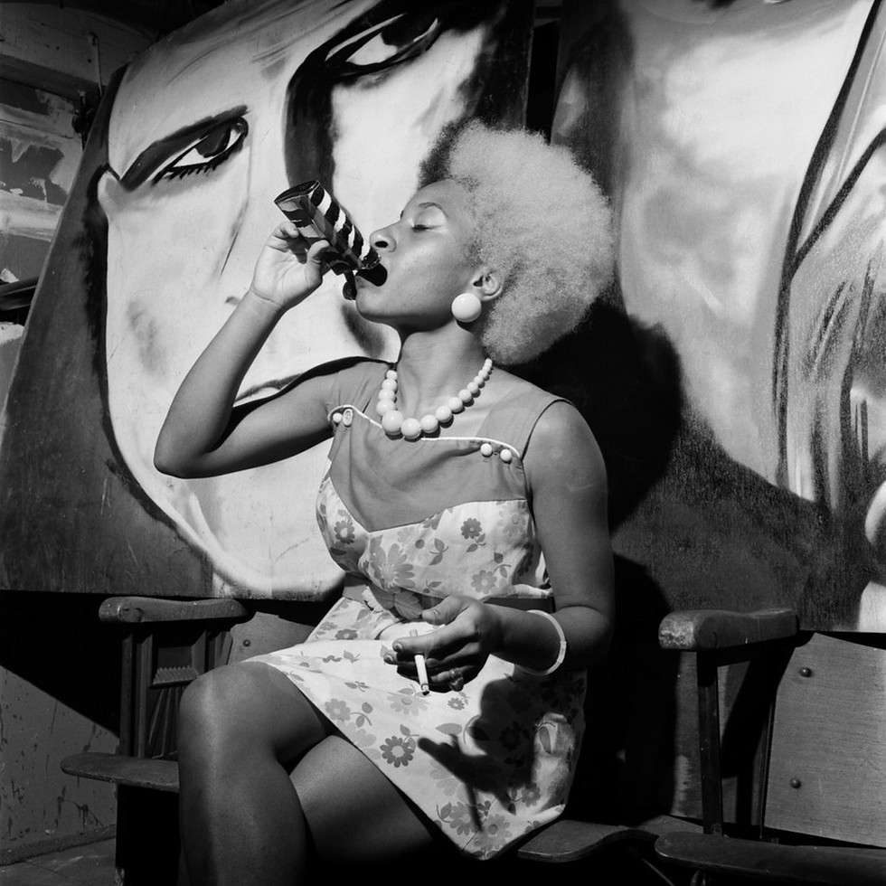 Thumbnail: Woman drinking in front of mural.