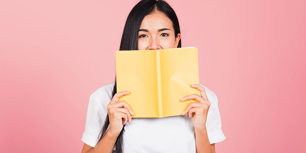 An Asian girl holds a book in front of her face, peeking over the top.