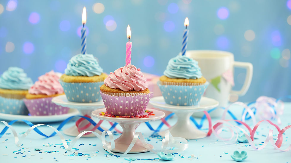 cupcakes piled high with frosting and topped with lit birthday candles sit on miniature cake stands.