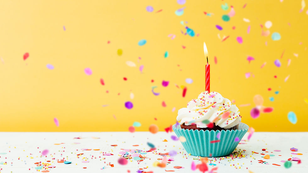 Cupcake with a ruffled wrapper, frosting piled high and a lit birthday candle