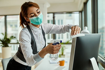 young-businesswoman-with-face-mask-disinfecting-her-desktop-pc-while-working-office-corona
