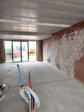 An unfinished interior space with exposed concrete walls and flooring. Electrical wires in blue, red, and white are coiled on the floor. Large sliding glass doors lead to an outdoor area.