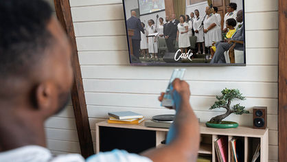 A man sitting in front of a TV watching a choir.