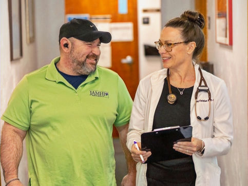 Two JAMHI staff members smiling and standing together in a clinic hallway, reflecting teamwork and community-care environment.