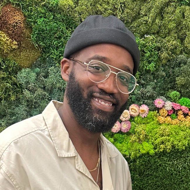 Big Mama Empanada co-founder Shawn smiling in front of a green plant wall