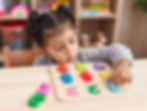 Adorable hispanic girl playing with maths puzzle game sitting on table at kindergarten