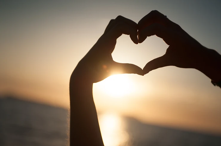 Two hands forming a heart at sunset