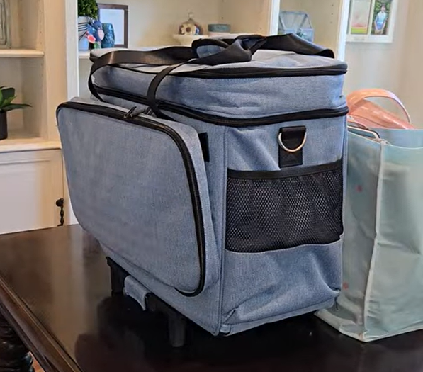 A rolling travel case for a sewing machine with all supplies inside and a tote bag with supplies too large for the travel case.