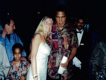 A man and woman stand side by side, smiling, at a lively party with colorful decorations in the background.