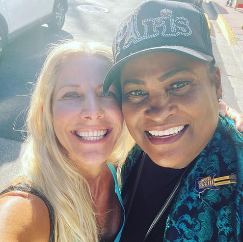 Two people happily pose for a selfie, both smiling widely, reflecting a joyful and friendly atmosphere.