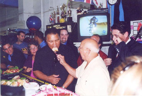 A man takes a bite of cake as an audience looks on, capturing a moment of celebration.