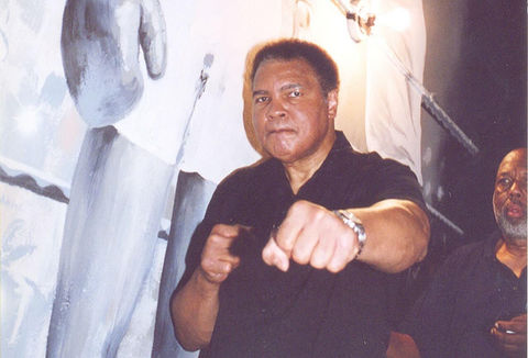 A man dressed in a black shirt and white pants gestures with his finger, indicating something off-screen.
