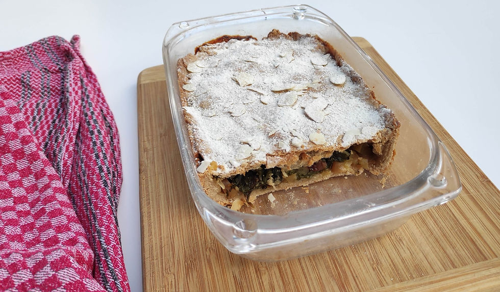 angeschnittener Mangoldkuchen mit Puderzucker in gläserner Auflaufform auf Holzbrett stehend; links: rotes Geschirrhandtuch