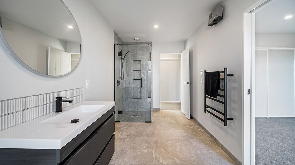 Modern bathroom with a large circular mirror, sleek black vanity, glass shower with gray tile, heated towel rail, and neutral color palette, designed by Kian Clements-Ormond.