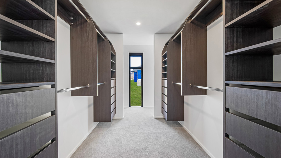 Spacious walk-in wardrobe, designed by Kian Clements-Ormond, with dark wood shelving, built-in drawers, and ample natural light from a full-length window.