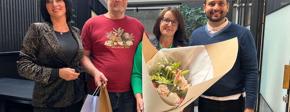 Happy clients celebrating their new home handover with the Hedgley Corporation team, holding flowers and gift bags in a modern interior.