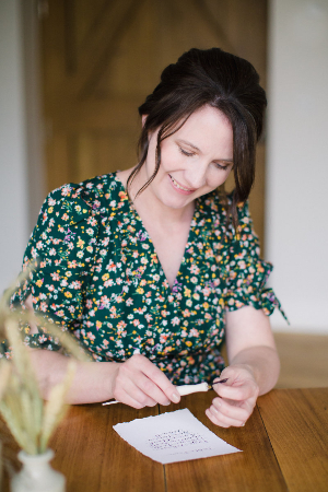 Lady in a green floral dress inserting nib in to a pen with a white page win front written in calligraphy