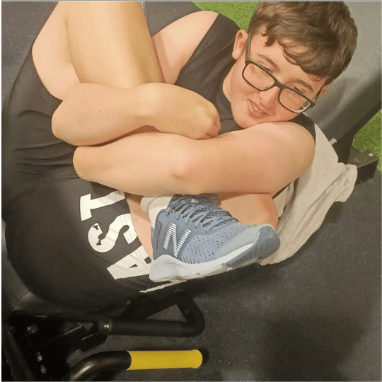 Neurodiverse teen curled up on a gym bench in a playful pose, smiling and relaxed.