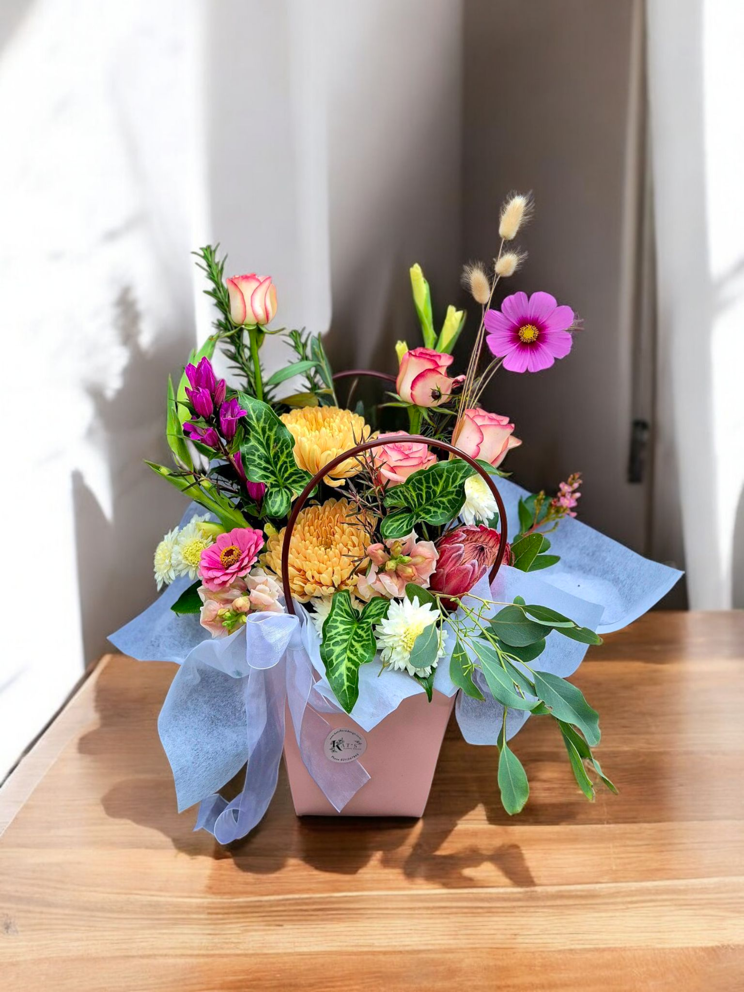 A soft pink pouch filled with seasonal flowers, tied with a matching ribbon.