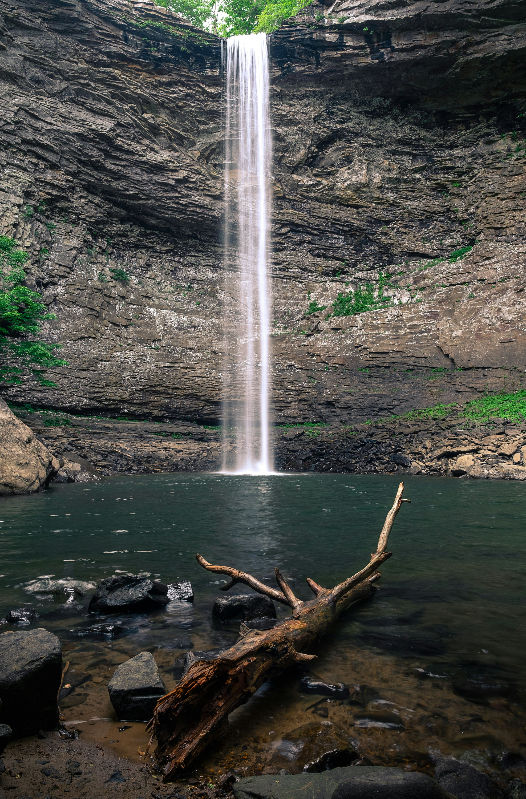 Tall waterfall pouring into a plunge pool at the bottom of a rock gorge, similar to the Cummins Falls swimming hole