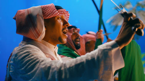 Traditional Saudi performer raising a sword on the blue-screen set for the King Salman Park film