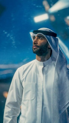Man in traditional Gulf clothing looking upward in a cinematic blue environment