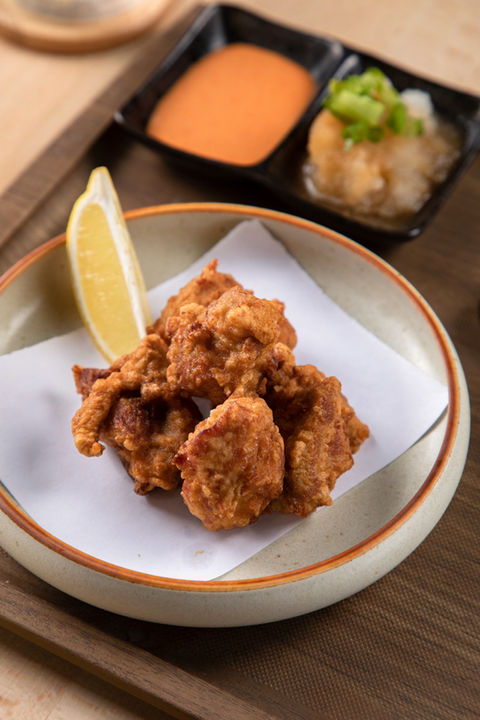 Fried chicken in bowl with lemon wedge, sauce and garnish on table.