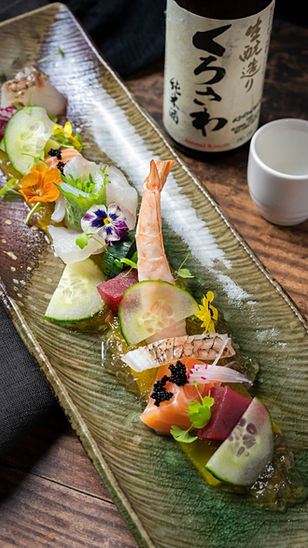 Sushi dish with fresh ingredients and a bottle of sake in background.