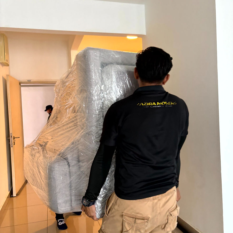 Two people move a plastic-wrapped sofa through a doorway in a bright room. One wears a black "AZIRA MOVERS" shirt.