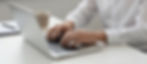 Hands typing on laptop keyboard at a desk with coffee.