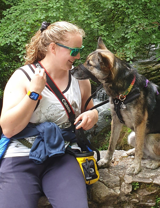 A woman and her dog sitting on a wall infront of a waterfall