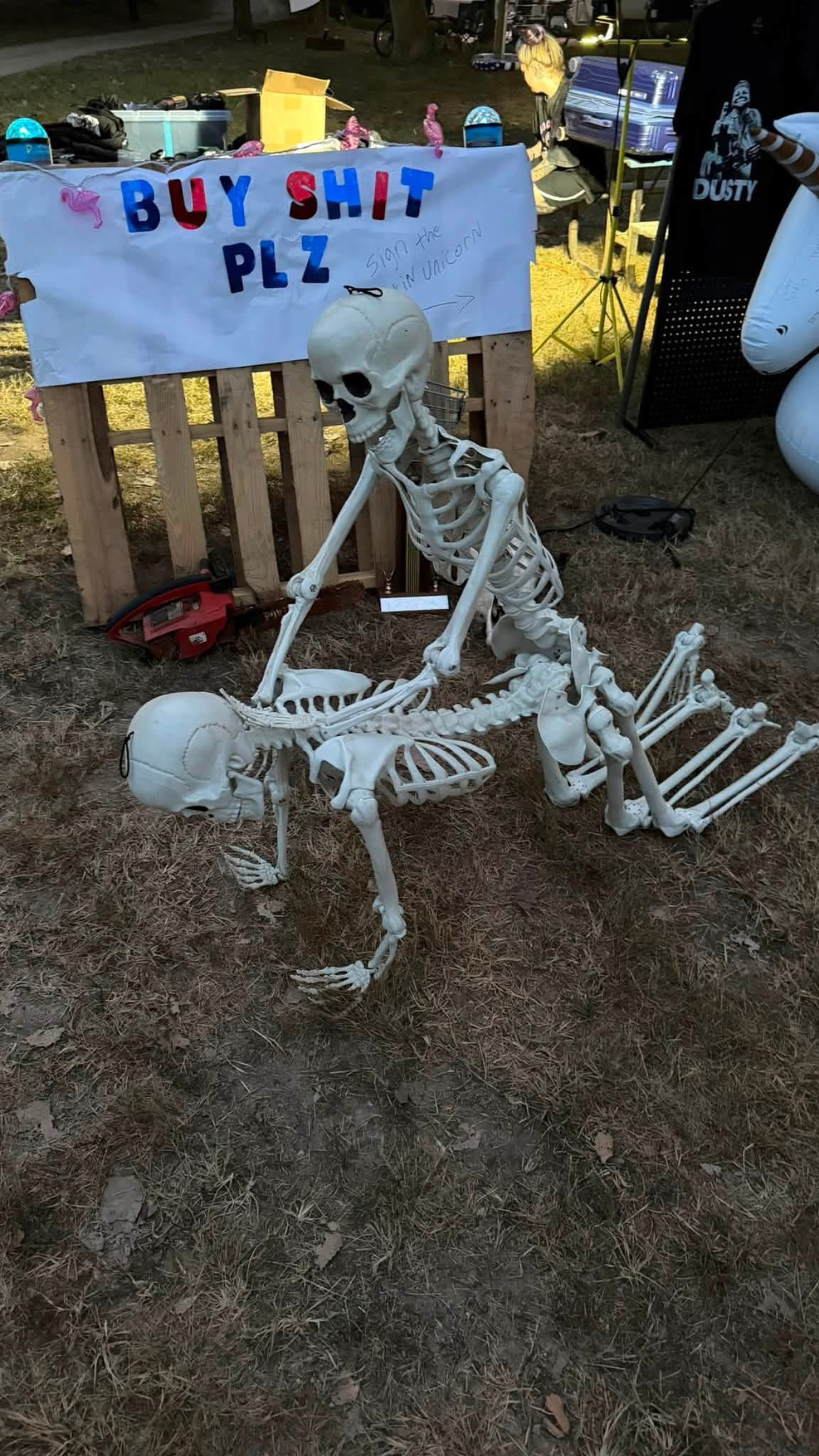 Skeletons beside a handwritten BUY SHIT PLZ sign.