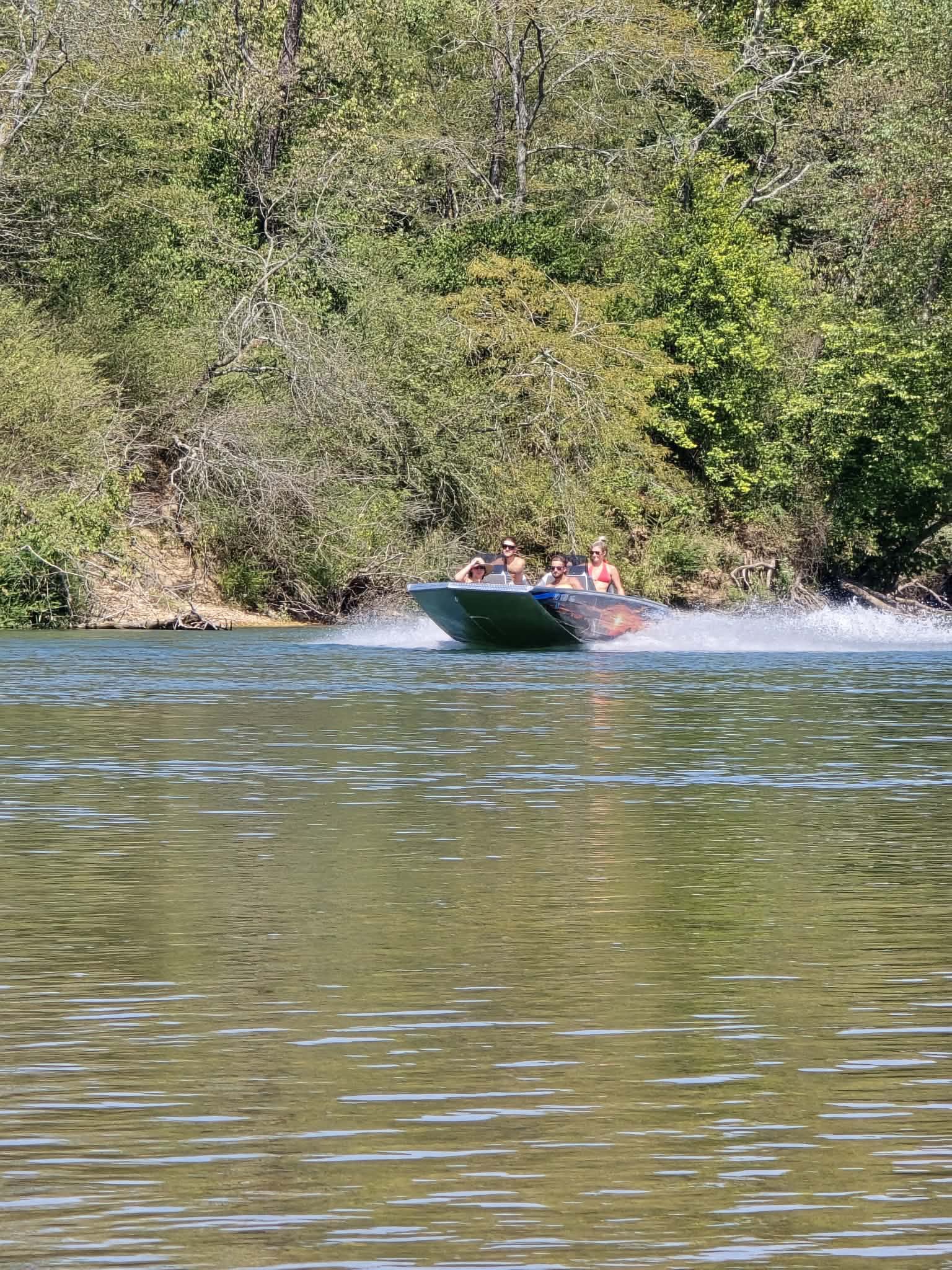 A boat on the Current River beneath a wooded bluff.