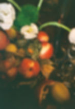 Still life with peaches, pears, and a pomegranate on ornate metal. White flowers and greenery add contrast. Warm, earthy tones.