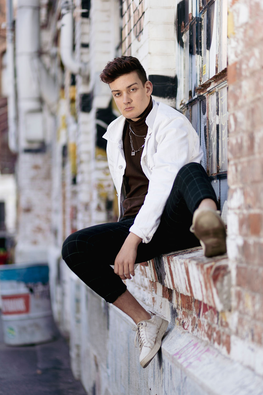 Junge Person sitzt vor einer Graffiti-Wand bei einem Portraitshooting