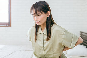 ベッドに腰かけ背中をおさえる女性