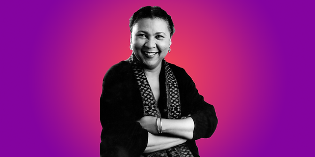 Image is of bell hooks smiling. Shown from the waist up with her arms folded in front of herself. In front of a purple to pink gradient background
