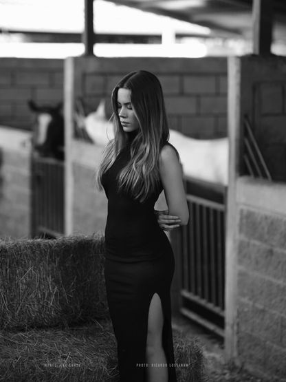 Retrato editorial en blanco y negro de una modelo con caballos en un establo de lujo.