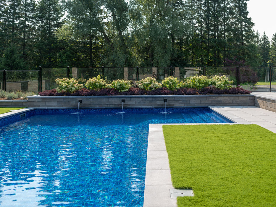 Close-up of a custom pool water feature with three sheer descent spouts integrated into a U-Cara stone planter with lush hydrangeas.